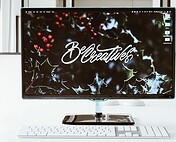 High-resolution computer monitor displaying "Be Creative" text with festive holly background for inspiring workspace decor.