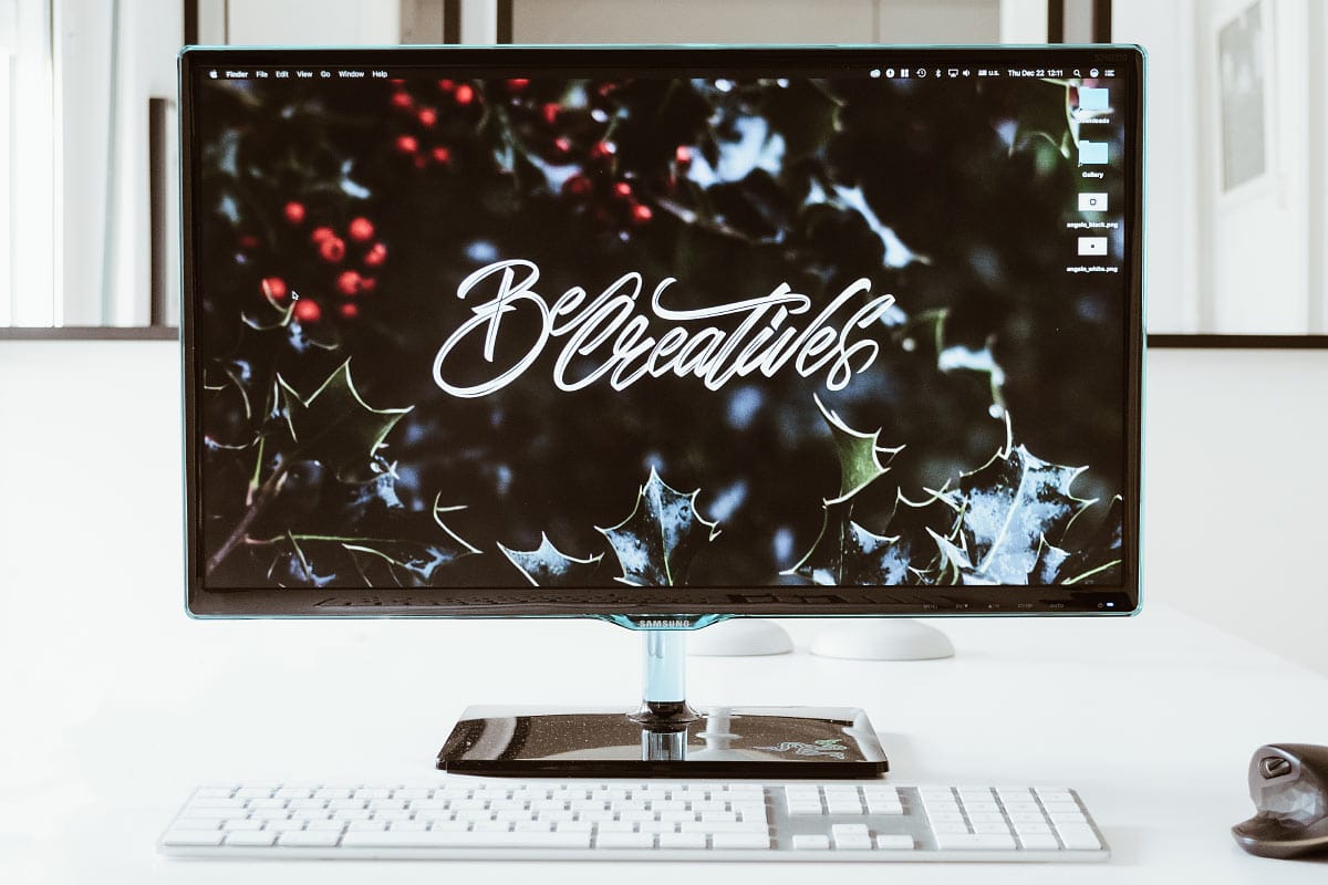 High-resolution computer monitor displaying "Be Creative" text with festive holly background for inspiring workspace decor.