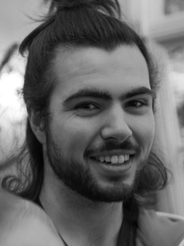 Portrait of a smiling young man with long hair and a beard, black and white photo.
