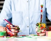 Vibrant paint-stained hands of an artist with brushes, showcasing creative process at Hoke Designs.