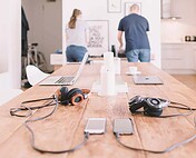 Modern home office with laptops, headphones, and smartphones on a wooden table, highlighting tech accessories and workspace organization.
