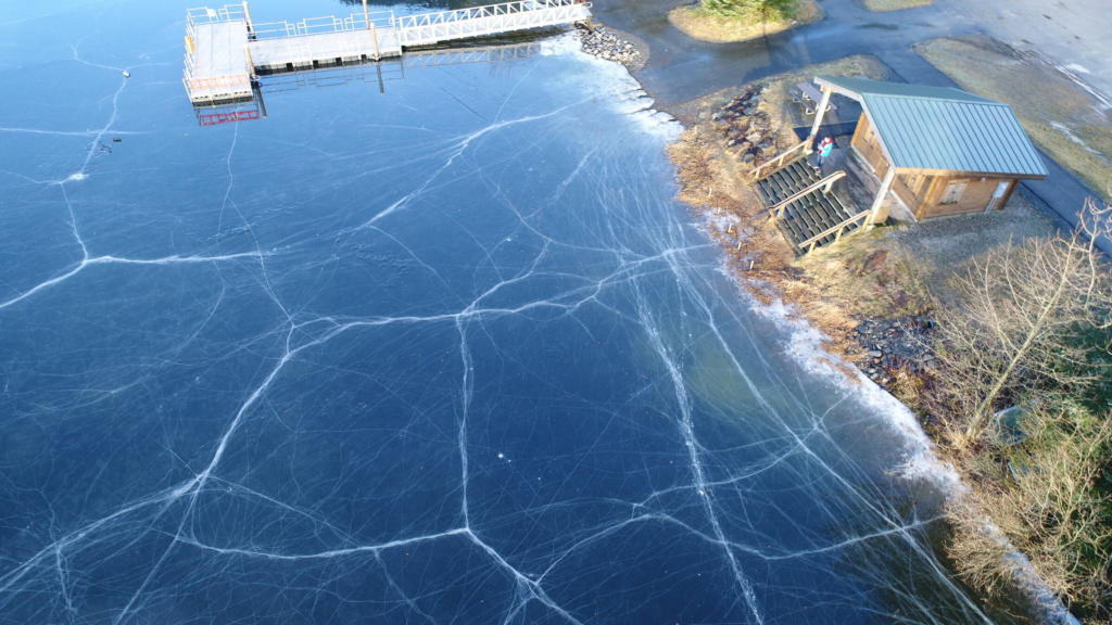 Overhead view of clear black ice with white crack lines and a dock