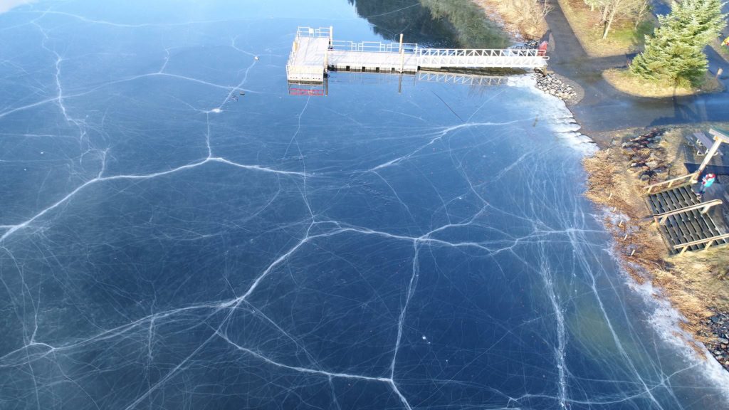Cracked black ice beside a dock and the shoreline
