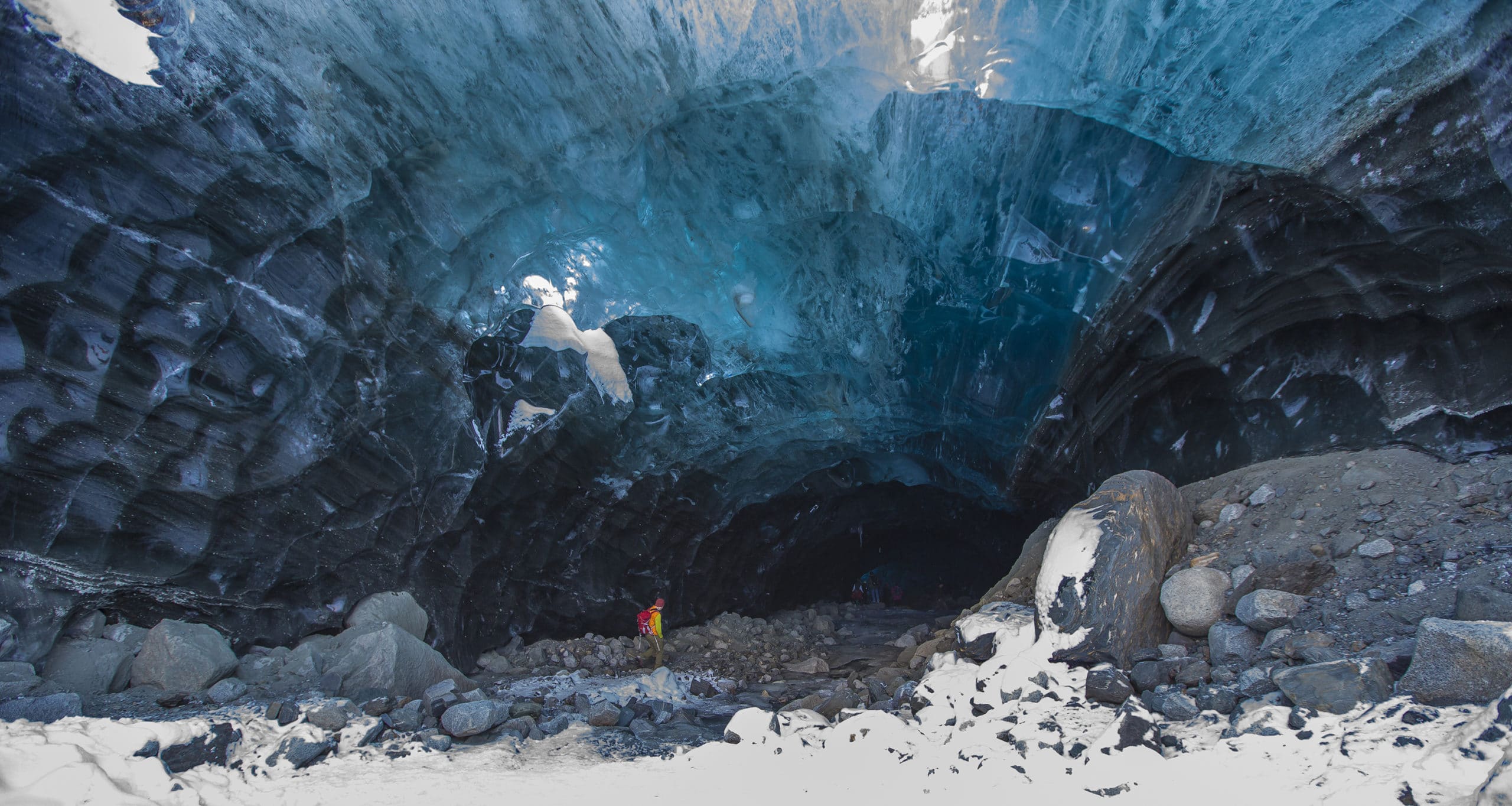 People exploring inside a stunning blue ice cave surrounded by rocks.