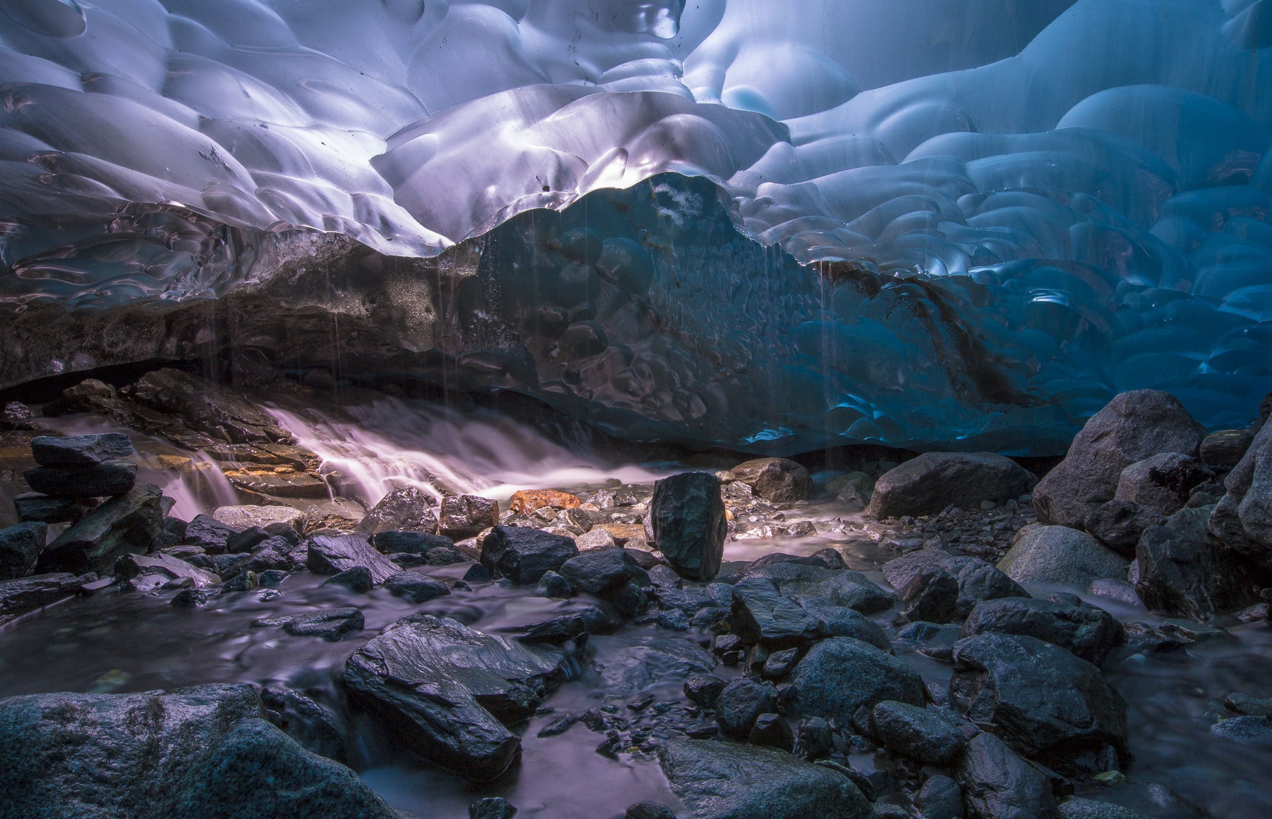 Bright blue ice formations inside an ice cave with water flowing through rocks and stones, showcasing adventure and glacier beauty.