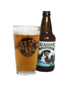 Alaskan Freeride APA bottle behind a pint of pale ale in a glass printed with the Freeride APA logo.