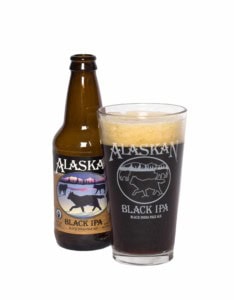 Alaskan Black IPA bottle beside a pint of dark beer in a glass printed with wolves, white background.