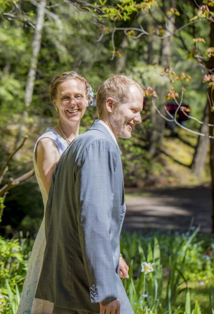 Smiling bride and groom walking through a sunlit garden, the bride looking toward the camera.