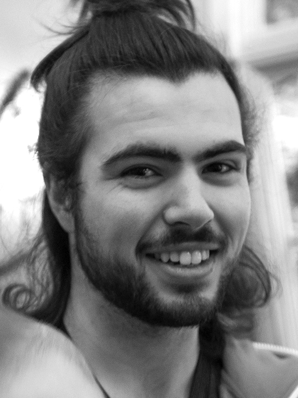 Smiling man with long hair, beard, and casual attire, showcasing relaxed style at Hoke Designs.