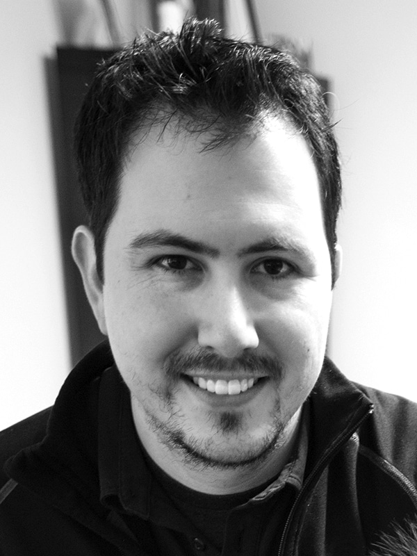 Portrait of a smiling man with dark hair, casual black jacket, in black and white.