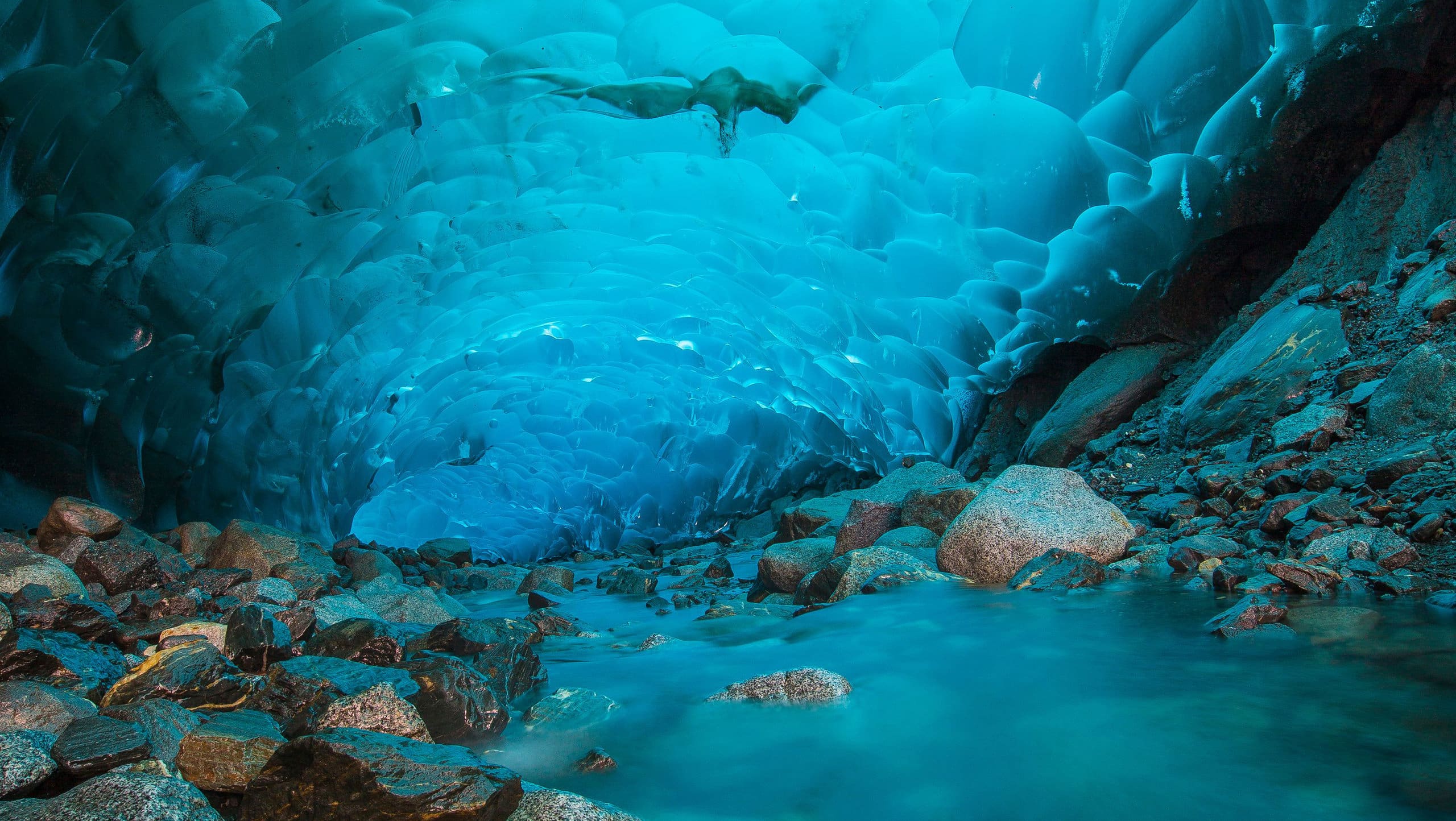 Stunning icy cave art with vibrant blue ice formations and rugged rocky surroundings.