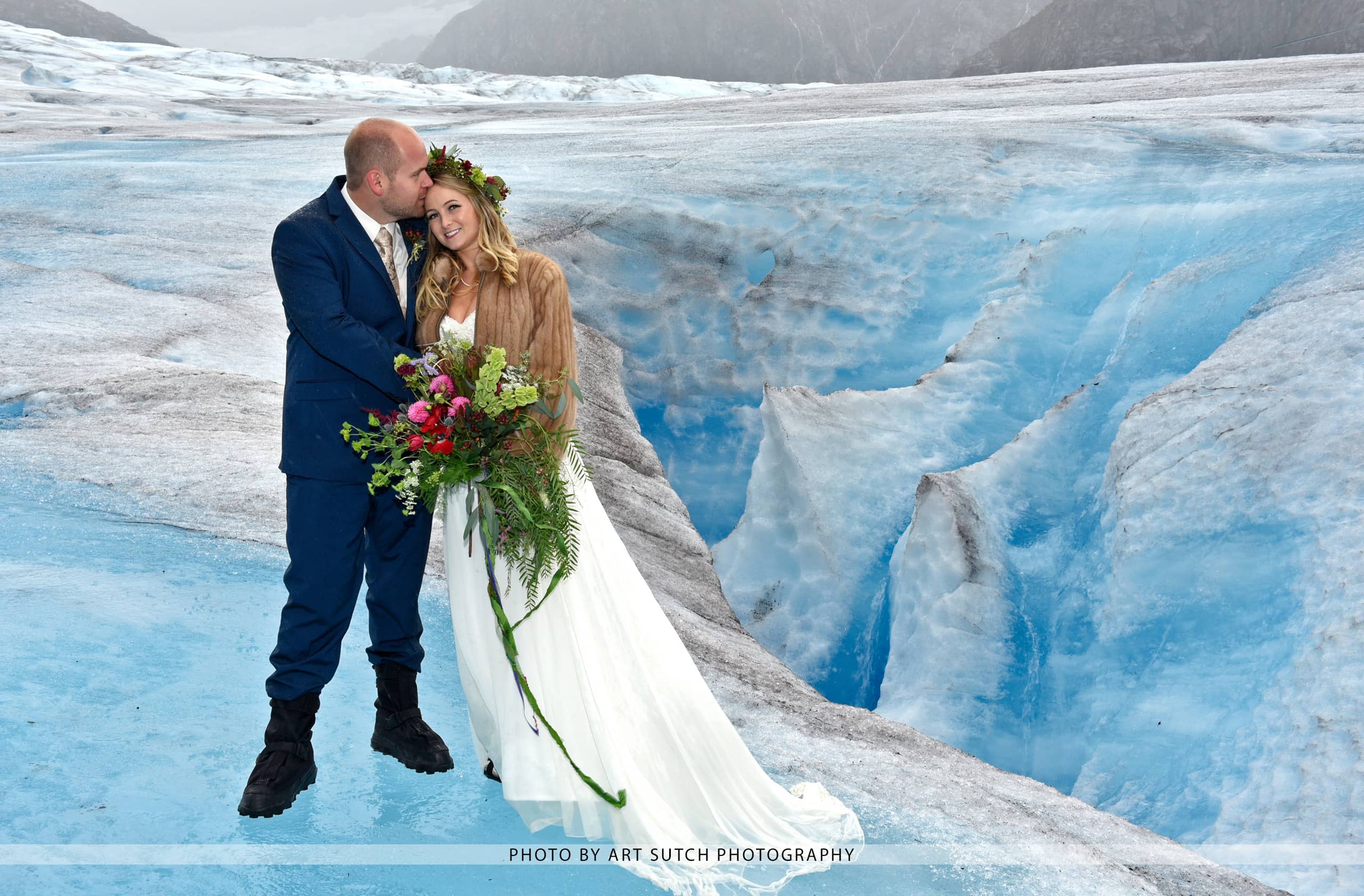 Couple in wedding attire holding flowers on icy glacier with blue ice formations.