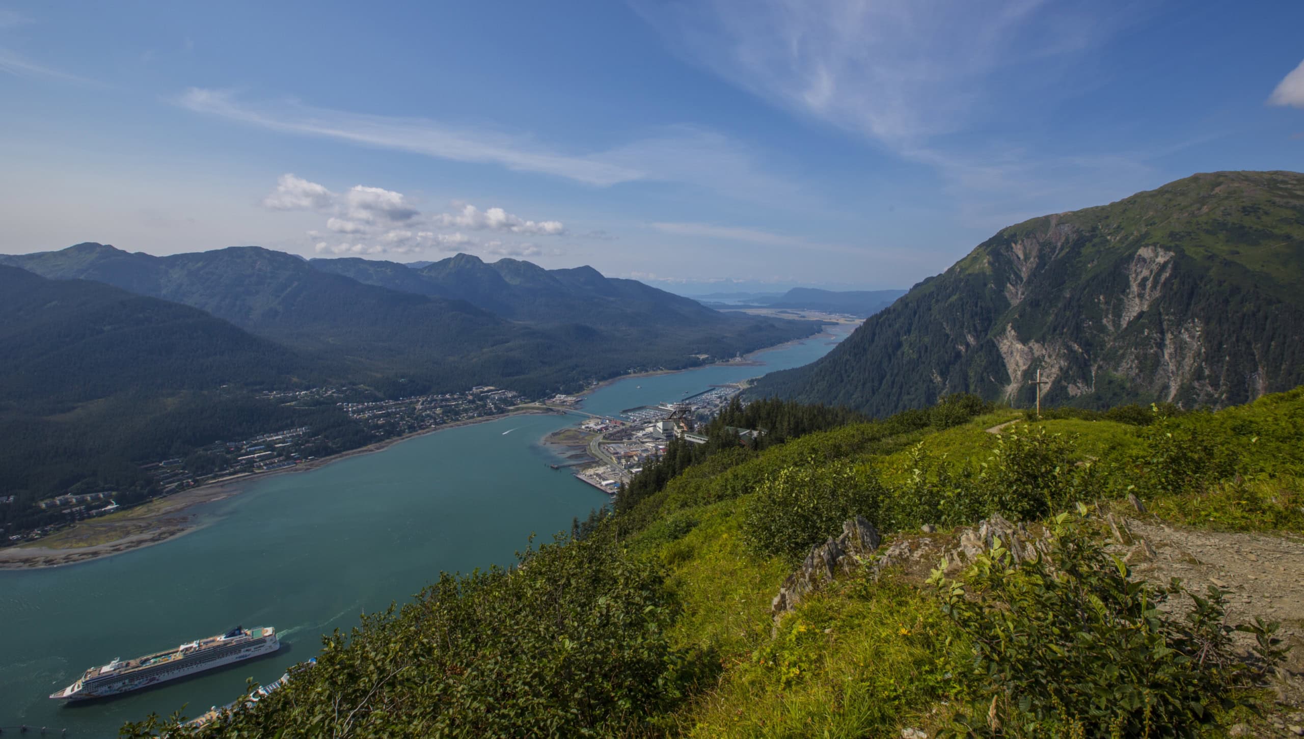 A panoramic view of a river winding through a lush green valley surrounded by majestic mountains, featuring a cruise ship sailing, ideal for travel and nature enthusiasts.