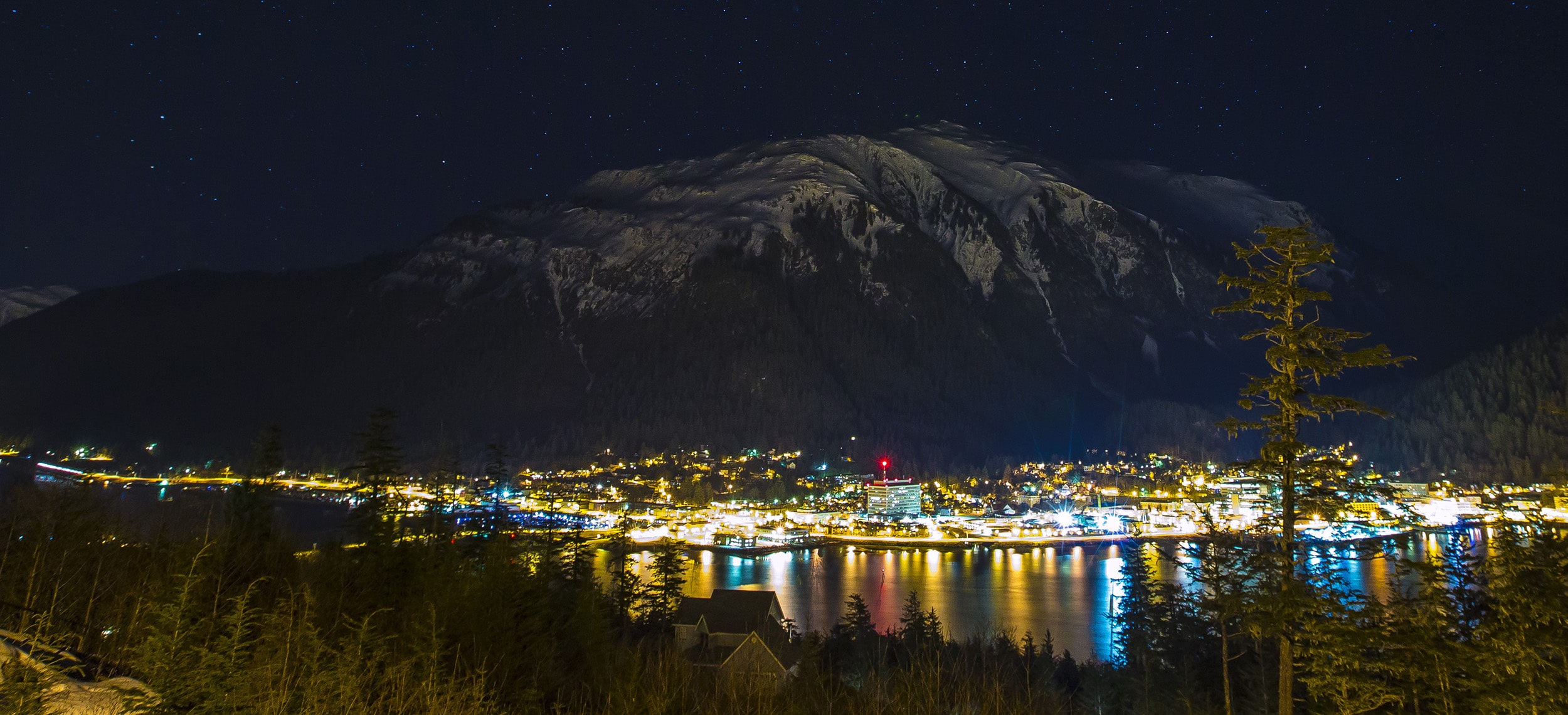 Nighttime photo of a mountain landscape with illuminated town and starry sky.