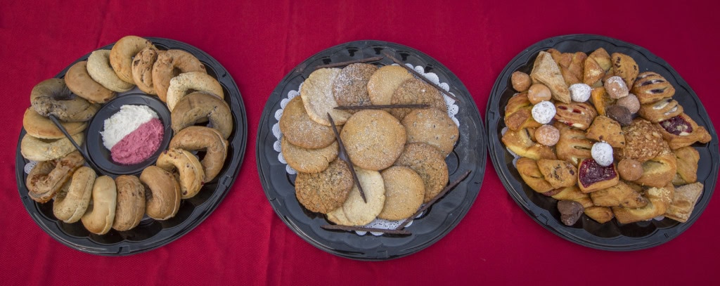 Overhead view of three trays on red cloth: bagels with cream cheese, cookies, and assorted pastries.
