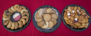 Overhead view of three trays on red cloth: bagels with cream cheese, cookies, and assorted pastries.
