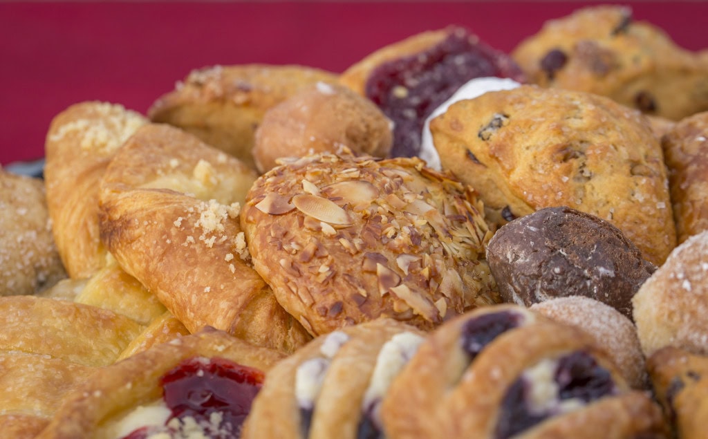 Close-up of an almond-topped pastry among scones, berry danishes and a chocolate donut hole.
