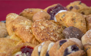Close-up of an almond-topped pastry among scones, berry danishes and a chocolate donut hole.
