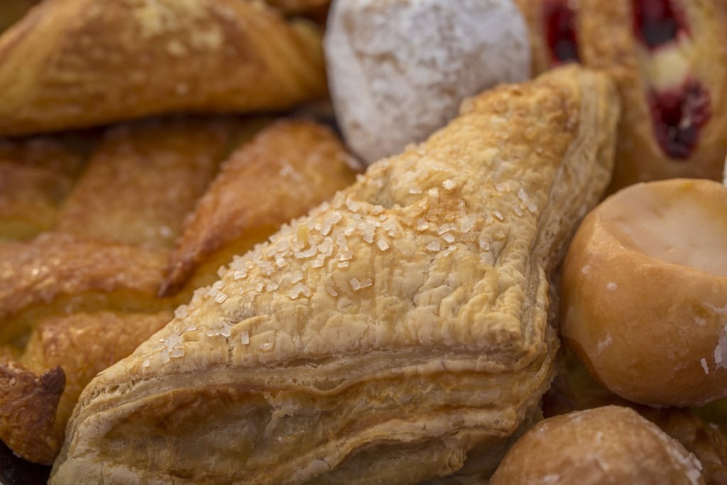 Close-up of a flaky sugar-topped turnover surrounded by danishes and powdered donut holes.