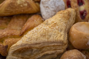 Close-up of a flaky sugar-topped turnover surrounded by danishes and powdered donut holes.