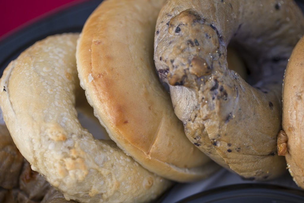 Close-up of three bagels, plain, golden egg and blueberry, overlapping on a tray.