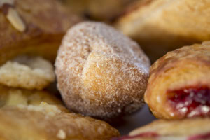 Close-up of a cinnamon-sugar donut hole surrounded by soft-focus pastries and a cherry danish.