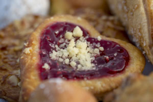 Close-up of a heart-shaped pastry filled with glossy red jam and topped with crumbs.