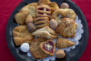 Overhead view of a tray of danishes, almond pastries, scones, a heart pastry and donut holes on a doily.