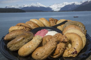 Bagel tray with berry and plain cream cheese in the center, snowy mountains, a glacier and water behind.