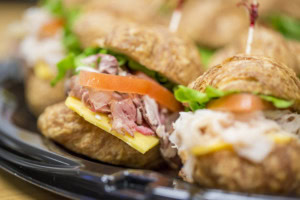 Close-up of croissant sandwiches with pulled ham, cheddar, tomato and lettuce on a black tray.