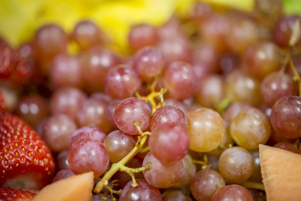 Close-up of red grapes on the stem with a strawberry and cantaloupe at the edges of the frame.