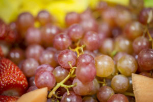 Close-up of red grapes on the stem with a strawberry and cantaloupe at the edges of the frame.