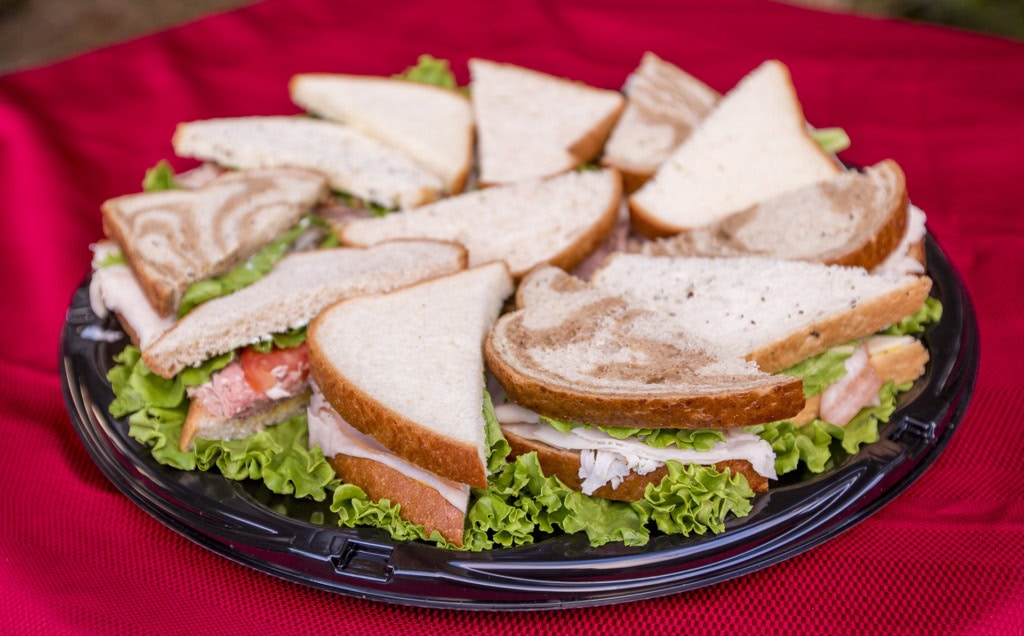 Platter of sandwich halves on white and marble rye bread with turkey, ham and lettuce on a red tablecloth.