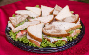 Platter of sandwich halves on white and marble rye bread with turkey, ham and lettuce on a red tablecloth.