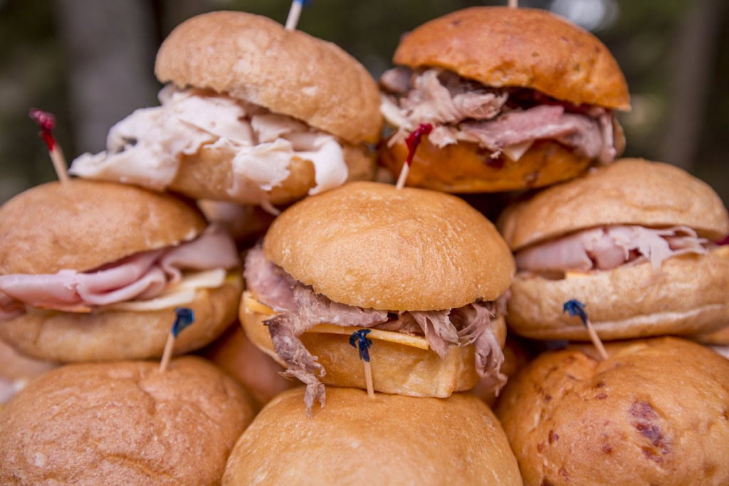 Close-up of stacked slider sandwiches with turkey, ham and roast beef on soft rolls with colored picks.