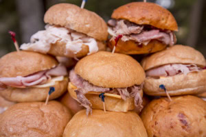 Close-up of stacked slider sandwiches with turkey, ham and roast beef on soft rolls with colored picks.