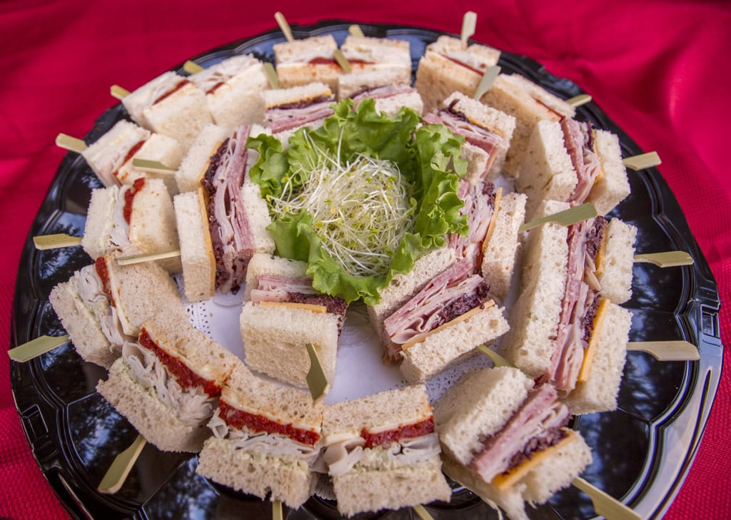Round tray of finger sandwiches with turkey and ham on bamboo picks, sprouts and lettuce in the center.