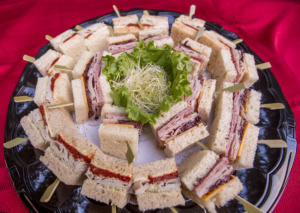 Round tray of finger sandwiches with turkey and ham on bamboo picks, sprouts and lettuce in the center.