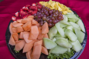 Fruit tray with cantaloupe, honeydew, red grapes, strawberries and pineapple on lettuce, set on a red cloth.