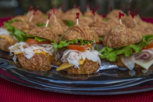 Close-up of mini croissant sandwiches with shaved turkey, cheese, tomato and lettuce on a black tray.