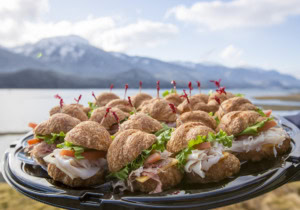 Platter of mini croissant sandwiches with turkey, ham, tomato and lettuce, snowy mountains and water behind.