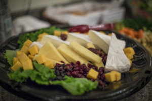Cheese tray with brie wedges, sliced and cubed cheddar, dried cranberries and blueberries on green leaf lettuce.