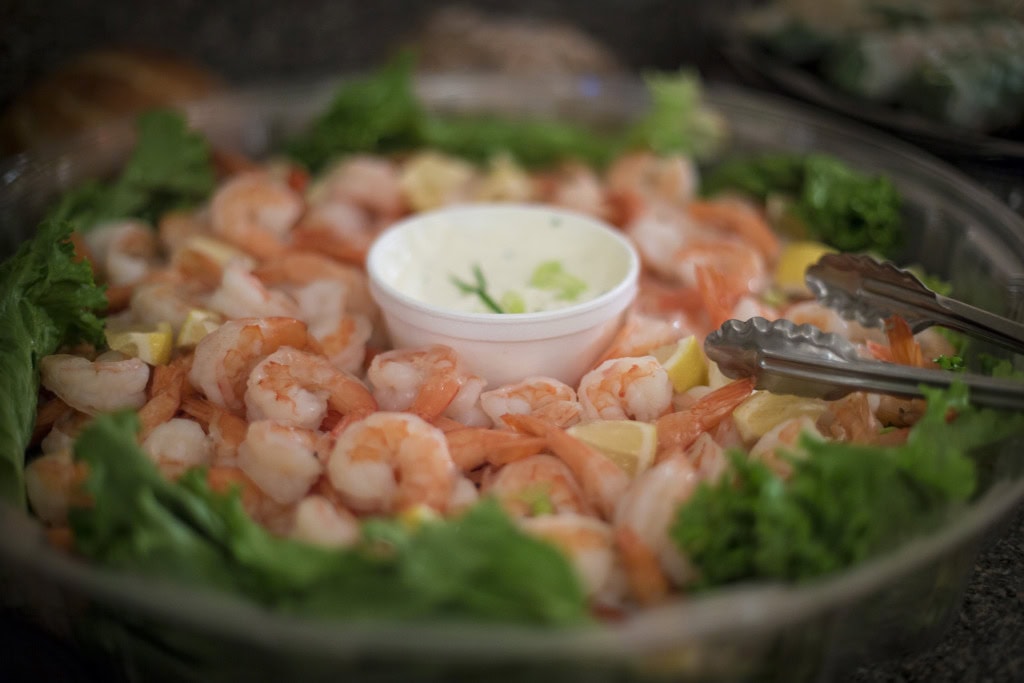 Platter of peeled shrimp with lemon wedges and lettuce around a cup of creamy dip, tongs resting on the side.