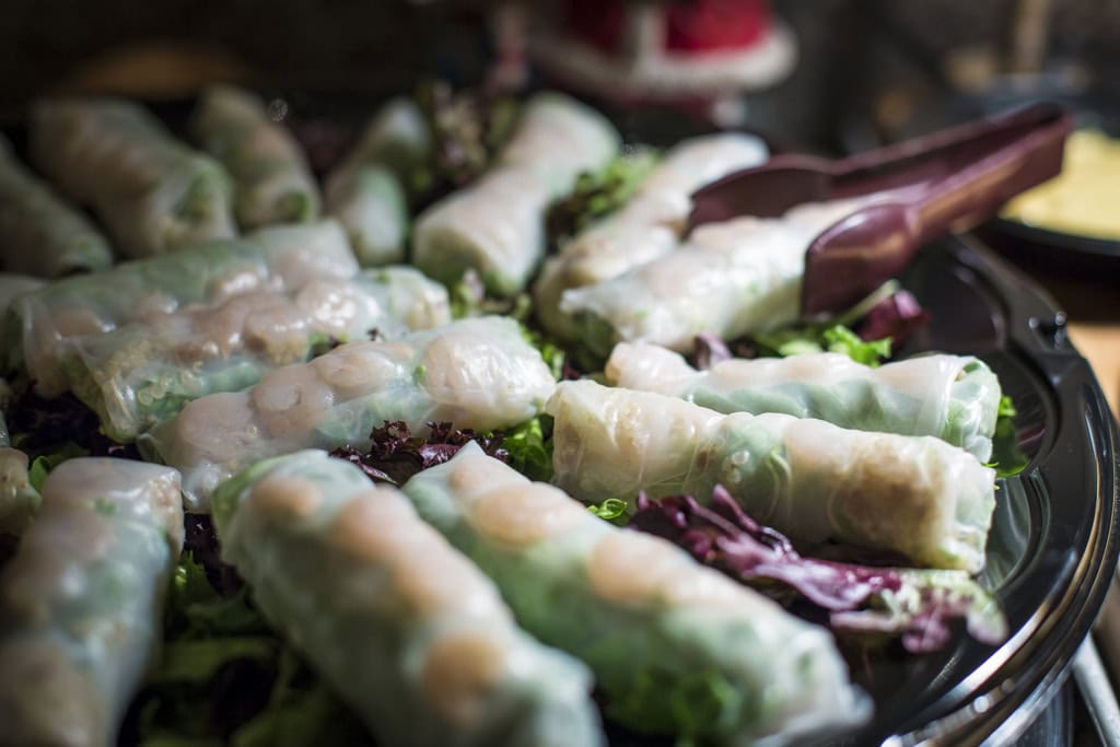 Rows of rice paper spring rolls with shrimp on red and green lettuce, serving tongs on the tray.