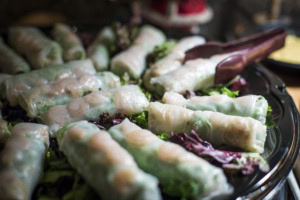 Rows of rice paper spring rolls with shrimp on red and green lettuce, serving tongs on the tray.