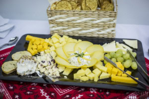 Cheese tray with cubed cheddar, sliced cheese, goat cheese, grapes and bread, a basket of crackers behind.
