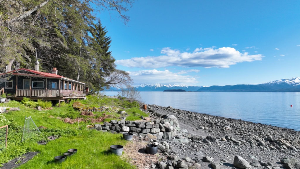 Cabin beside a rocky shore with mountains across the water