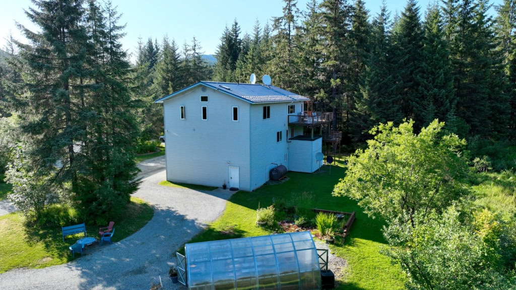 A white two-story house with a greenhouse in a forest clearing