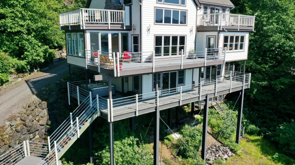 A tall white home with multiple decks and exterior stairs set into a forested hillside