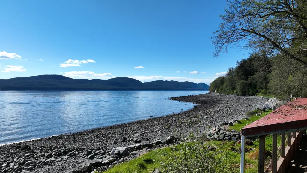 Calm blue channel, distant islands and a rocky beach seen from beside a cabin porch